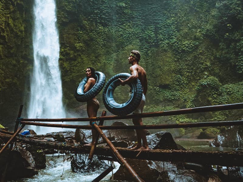 a man and a woman with inner tubes near a waterfall and river