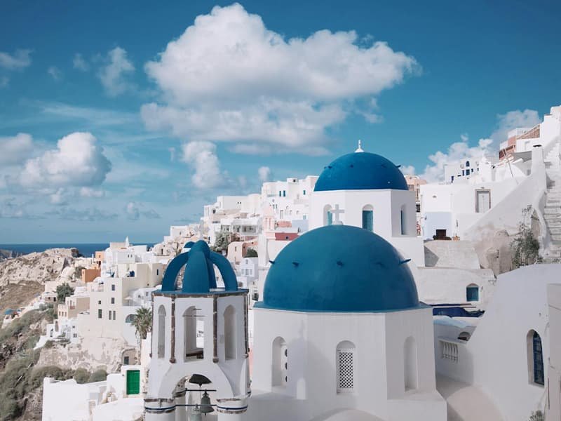 A daytime view of Santorini, Greece on a bright, sunny day with bright white clouds