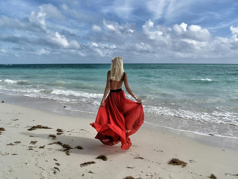 Woman in a red flowing skirt walking on the shoreline of a beach